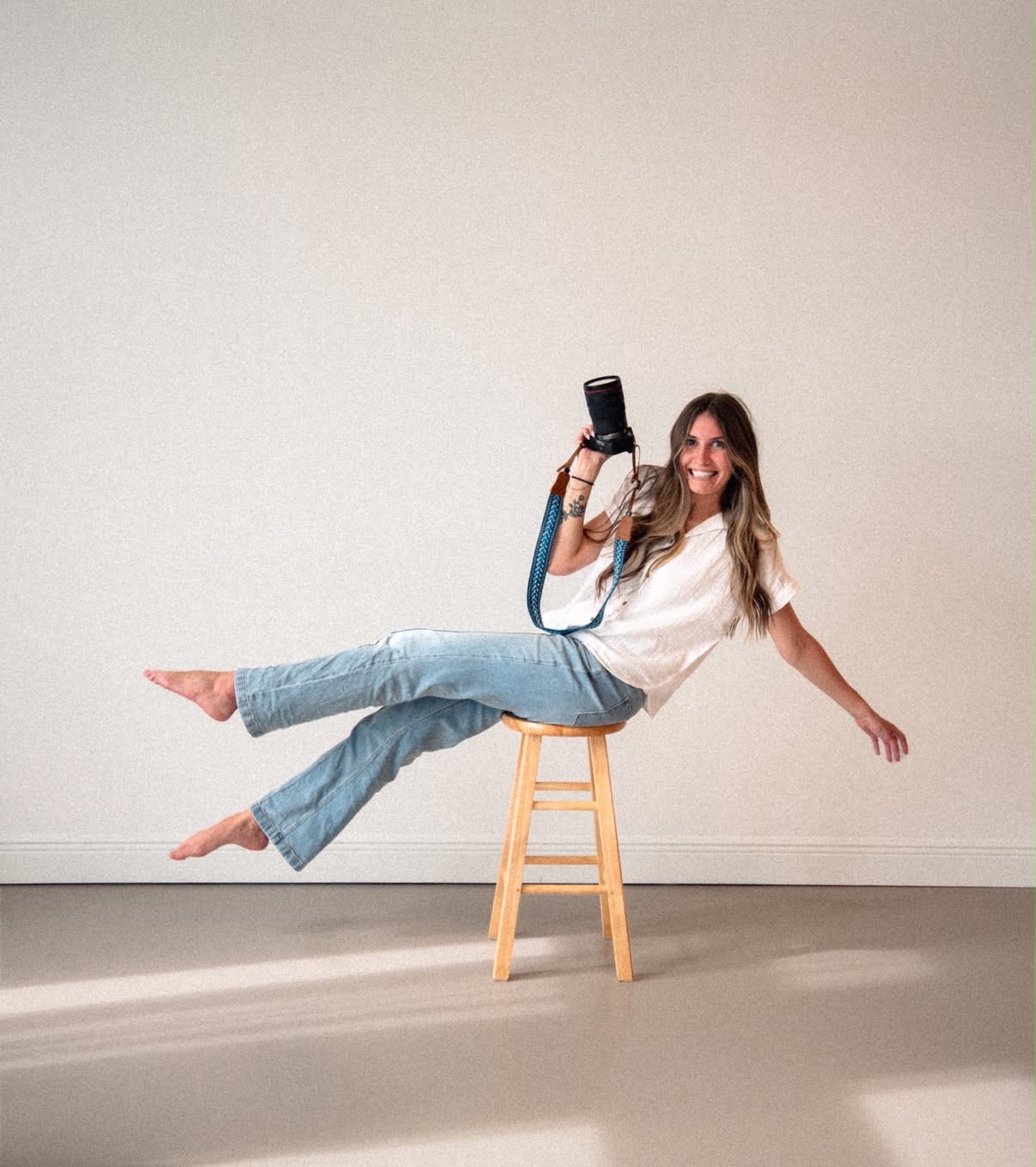 Cloe sitting on a stool holding her camera in soft natural light