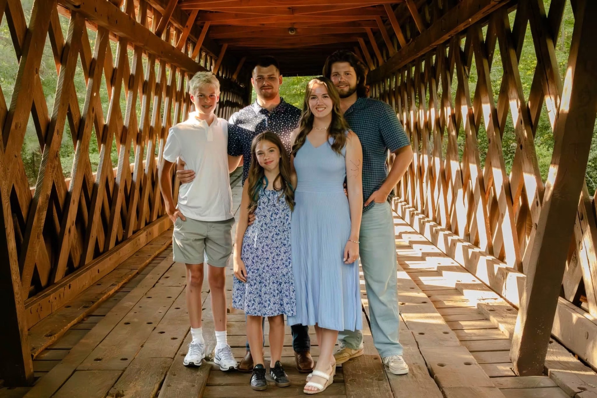 Family of five standing together inside a covered wooden bridge